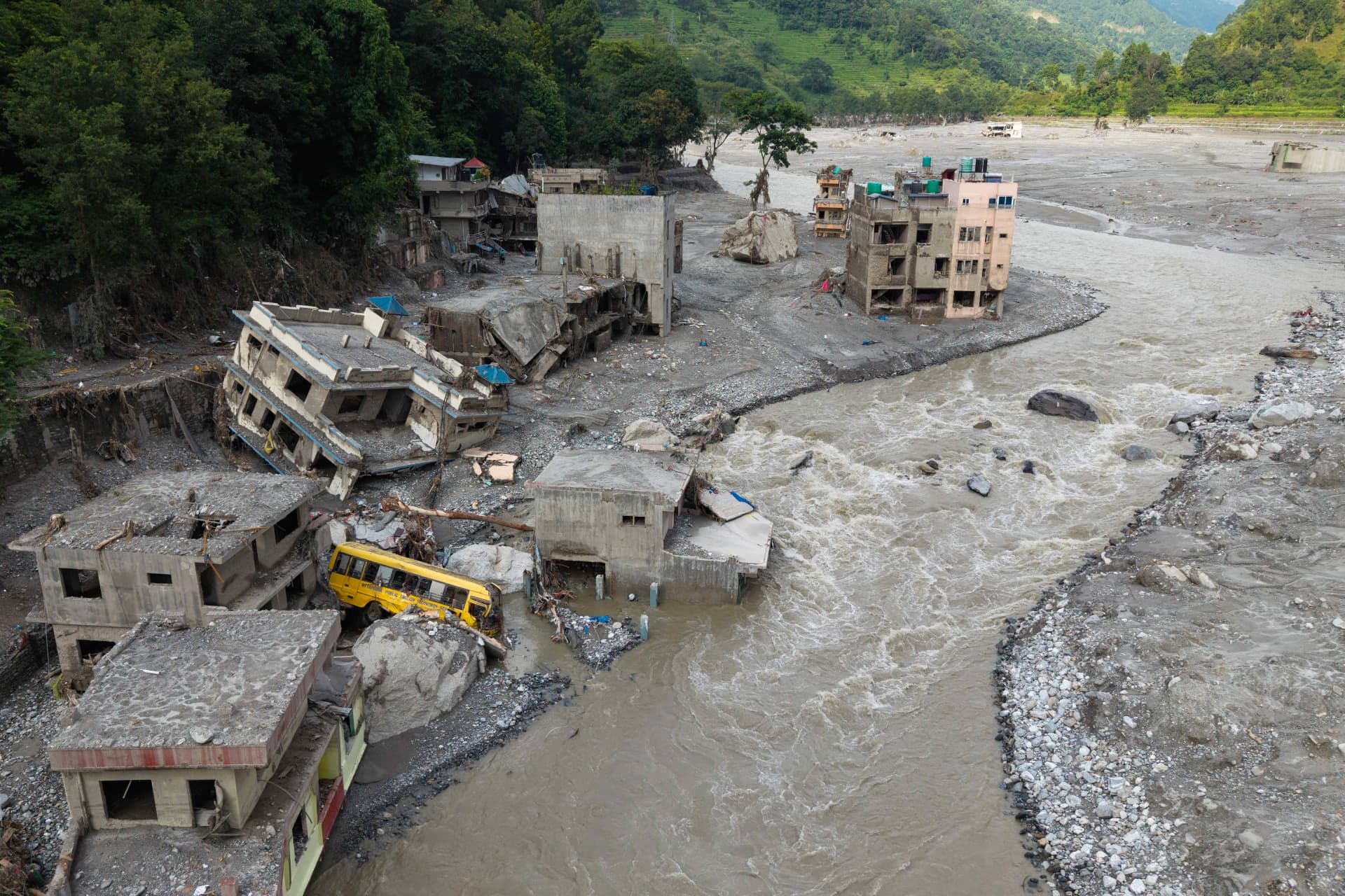 Aerial view of a Nepali town destroyed by flash flooding, with a school bus buried in debris