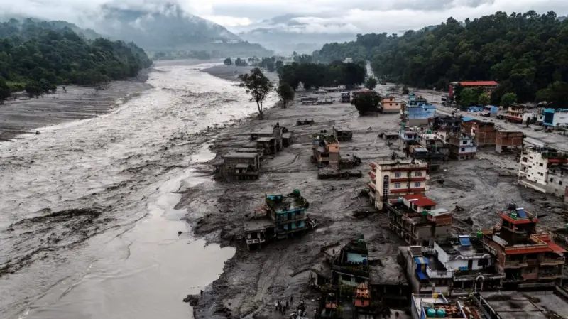 Homes surrounded by grey silt along a swollen river in Nepal